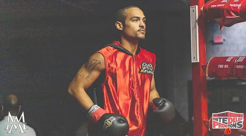 Jeremiah in a red walkout vest and gloves, waiting in the back before a fight
